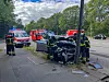 Feuerwehrkräfte begutachten den beschädigten BMW. Der Lichtmast ist durch den Unfall verbogen worden.