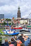 Schaulustige beobachten mehrere Schlepper beim traditionellen Schlepperballett auf der Elbe vor den Landungsbrücken und dem Stadtpanorama.