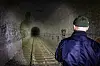 Eine Person steht in einem beleuchteten Tunnel mit Gleisen und Ziegelwänden.
