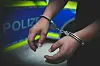 Hände in Handschellen vor Polizeiwagen