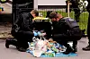 Polizisten durchsuchen auf der Suche nach Hinweisen eine Mülltonne.