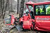Ein schwer beschädigter kleiner Schultransporter steht am Straßenrand neben einem Baum. Teile des Fahrzeugs wurden durch eine Kollision abgetrennt. Im Hintergrund stehen Rettungsleute.