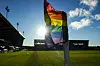 Eine Eckfahne mit Regenbogen-Flagge wird von der Sonne angestrahlt.