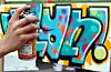 Eine Hand hält ein Grafitti-Spraydose vor einer besprühten Wand.