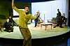 Szene aus dem Stück. Vorne Hegemann stehend, hinten im Raum fünf Schauspielerinnen und Schauspieler sitzend