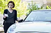Eine junge Frau an ihrem Auto, sie hält einen Strafzettel in der Hand