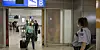 Reisende mit Mundschutz am Athener Flughafen. Fragt sich, auf wen zukünftig ein Corona-Test wartet und auf wen nicht.