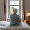 Eine ältere Frau sitzt auf einem Bett.