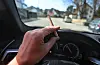 Ein Mann sitzt mit einem Joint zwischen den Fingern am Steuer eines Autos.