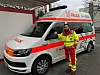 Junger Mann in Sanitäter-Anzug vor einem Krankenwagen
