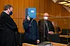 Der Hauptangeklagte steht zwischen seinen Anwälten und verdeckt sein Gesicht mit einer Mappe.