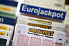 Eurojackpot-Spielschein liegt vor einem Eurojackpot-Werbeschild und ausgefüllten Zahlenfeldern.