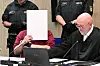 Der Angeklagte in einem Mordprozess nach einer Todesfahrt von Mannheim sitzt mit einem Aktendeckel vor seinem Gesicht im Gerichtssaal, rechts neben ihm sitzt sein Verteidiger Uwe Kosmala.