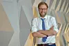 Verkehrssenator Anjes Tjarks (Grüne) steht mit verschränkten Armen vor einer Wand und lächelt in die Kamera.