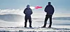 Zwei Männer stehen im Schnee und blicken auf einen rosa Jet.