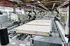 Roboter fertigen in einer Fabrikhalle Bauteile eines Mietshauses.