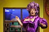 Der Schauspieler ist als Frau gekleidet, auf dem Kopf lila Plastiklocken und aus dem lila Kleid fallen beinahe die Brüste raus