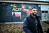 Agit Kabayel steht vor einem Graffiti was ihn selber zeigt