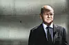 Bundeskanzler Olaf Scholz schaut in die Ferne, hinter ihm graue Zementwand.