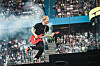 Im Hintergrund Publikum, vorne Sheeran mit Gitarre, der auf ein Podest hübpft
