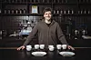Junger Mann vor Kaffeemaschine mit Kaffeebechern vor sich