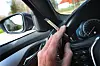 Ein Mann sitzt mit einem Joint zwischen den Fingern am Steuer eines Autos.
