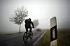 Ein Radfahrer fährt durch dichten Nebel auf einer Landstraße.