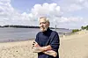Kapitän Schwandt stehet in typischer Pose mit Zigarette im Mund an einem Strand. Im Hintergrund ist Wasser zu sehen.