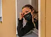 Eine junge Frau mit Maske schaut aus dem Fenster.