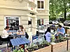 Menschen sitzen an einem Straßencafé vor historischem Gebäude und essen im Freien.
