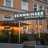 Schweinske-Restaurant mit Biergarten und Lichterketten an einer Straßenecke am Abend.