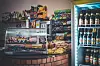 Kiosk mit Glasvitrine, Snacks, Süßwaren und Getränken in Regalen und Kühlschränken.