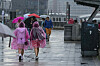 Touristen mit Regenschirmen unterwegs im Regen an den Landungsbrücken im Hafen.