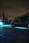 Zwei getunte Fahrzeuge mit blauer Neon-Unterbodenbeleuchtung driften nachts über das oberste Deck eines Hamburger Parkhauses, während Zuschauer im Hintergrund zuschauen.