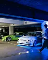 Nachbauten eines grünen Mitsubishi Eclipse und eines weißen VW Jetta aus dem ersten „Fast & Furious“-Film stehen beleuchtet in einem Hamburger Parkhaus.