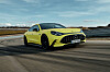 Gelber Mercedes-AMG GT 4-Türer fährt auf einer Teststrecke. Die elektrische Limousine zeigt den großen Panamericana-Grill und die flache Coupé-Silhouette.