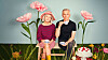 Eine Frau und ein Mann sitzen auf einer Holzbank zwischen großer Blumen.