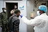 Ein Mann in Schutzanzug misst bei einem anderen Mann Fieber