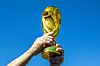 Hände halten einen goldenen WM-Pokal vor blauem Himmel.