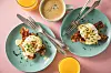 Wie ein Schuss flüssiges Gold fließt die Hollandaise bei Eggs Benedict über pochierte Eier auf Bacon und halbierten englischen Muffins.