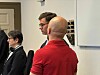 Der Angeklagte trägt ein rotes Kurzarm-Shirt und steht mit dem Rücken zur Kamera.