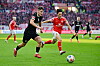 Arkadiusz Pyrka von St. Pauli im Zweikampf mit Jae-Sung Lee von Mainz vor einer TV-Kamera von DAZN