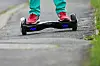 Ein Junge fährt mit einem Hoverboard auf einem Gehweg.