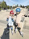 Zwei Mädchen stehen auf Inlineskates im Skatepark und jubeln.