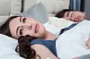 Eine junge Frau liegt wach neben ihrem Partner im Bett.