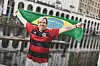 Brasilien-Fan hält eine Fahne vor einer spiegelnden Wasserfläche und feiert die Fußball-WM