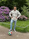 Japan-Fan steht im Park mit einem Fuß auf einem bunten Fußball vor blühenden Sträuchern