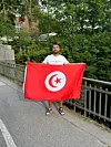 Tunesien-Fan hält eine rote tunesische Flagge mit Halbmond und Stern auf einem Gehweg an einer Brücke
