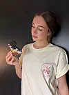 Junge Frau im hellen T-Shirt hält ein dekoriertes Eis vor dunklem Hintergrund.