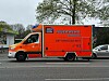 Rettungswagen der Hamburger Feuerwehr in Rot-Weiß mit Blaulicht auf der Straße.